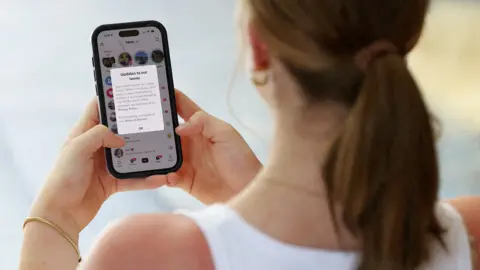 An unidentifiable young girl holds a phone with the TikTok app open showing a notification saying 'updates to our terms' to include banning younger users in Australia, taken in Sydney on Thursday.