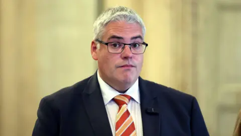 PA Media A man with white hair and glasses in a suit standing inside. 