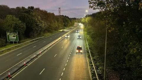 Landscape view of cars travelling on the A63 dual carriageway at dusk with the Humber Bridge in the distance.