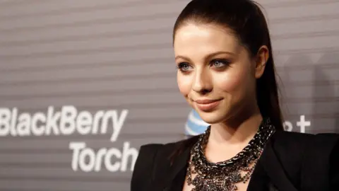 Actress Michelle Trachtenberg poses at the party wearing a black dress and necklace.