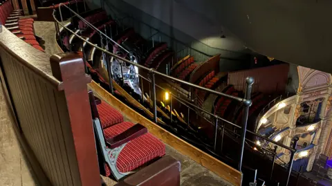 BBC/Richard Moss The Gallery of the Tyne Theatre and Opera House. Red seats with wooden backs and black metalwork look down towards the elaborately-decorated theatre boxes.