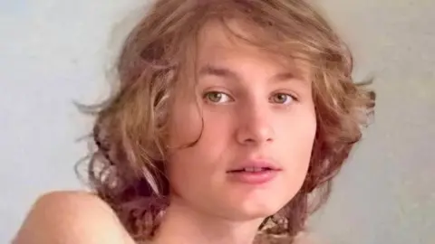 Daniel has medium length brown hair and is looking at he camera