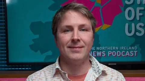 A man is looking into the camera, he has a slight smile on his face.