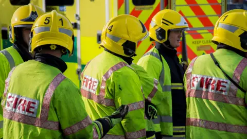 Getty Images Fire fighters gather wearing protective clothing and hard hats.