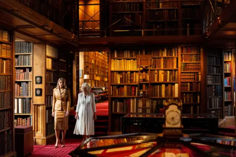 Aaron Chown/PA Wire First Lady Melania Trump, wearing a light-brown leather two piece skirt suit, and Queen Camilla, wearing a mid-length white dress with blue stripes, walking through the Royal Library at Windsor Castle, Berkshire
