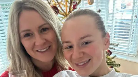 Jane Coates is standing next to her daughter Lucy Harrison is a selfie taken in front of a Christmas tree in the living room. 