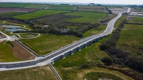 An aerial view of the road which is surrounded by fields with hedges and trees.