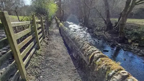 Bradford Council A path runs beside a wall adjacent to a river