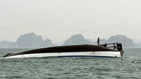 AFP A man stands on an upturned tourist boat that capsized in Ha Long Bay, Quang Ninh province, Vietnam. 