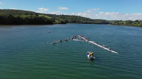 Several rowers are pictured positioning their boats to create an "A" shape for Alastair Barr.