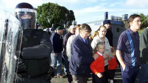 PA Media Archive image of the Ardoyne Holy Cross dispute, with riot police shielding parents and children walking along the road to school