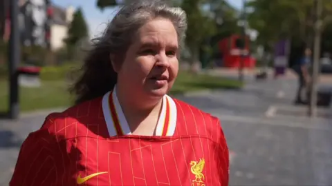A female Liverpool fan in a red jersey - she is middle aged with blonde hair 