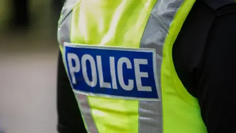 A stock image of the back of a police officer's uniform. It is a close up of a reflective jacket with the word "Police" on it.