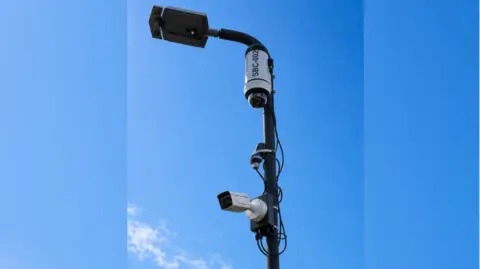 A pole with a CCTV camera on it against a blue sky.