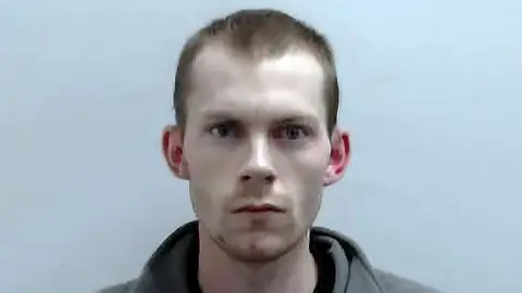 Police Scotland Close-up portrait of Connor Manners. He is facing the camera against a plain light background, with very short hair and wearing a grey top.