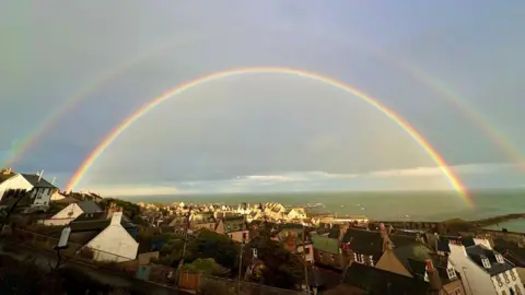 Magi Allan Double rainbow arc over a town, with the sea in the distance.