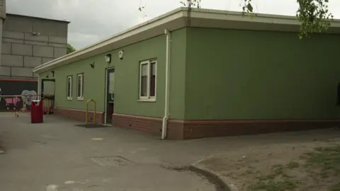 The classrooms are in a green, flat roofed building. 