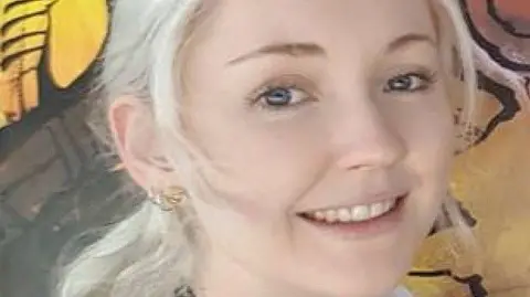Queensland Police Service A close-up image of a woman with blonde hair and blue eyes smiling at the camera.