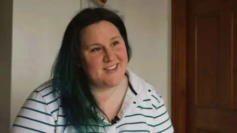 Dominique Shepherd, who has dark hair and dark eyes. She wears a white and green-striped rugby jersey.