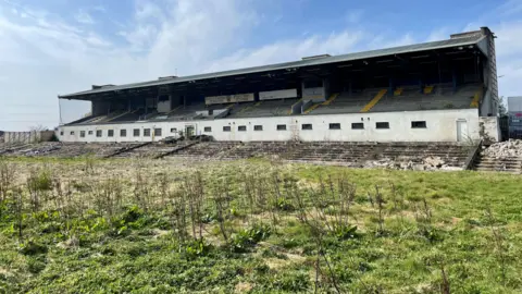 PA Media A run down stadium. Overgrown grass is in the foreground.