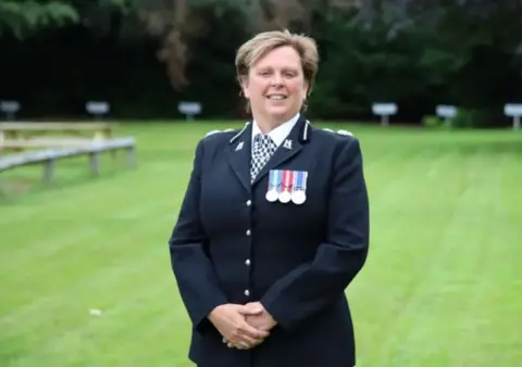 A smiling, female police officer in uniform standing on a lawn