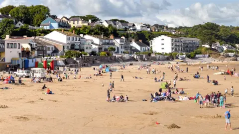 Getty Images Groups of people enjoy the sunshine on a sandy beach with homes lining the front