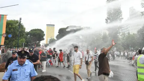 A policeman and a large group of people being hit by a jet stream from water cannon in a street