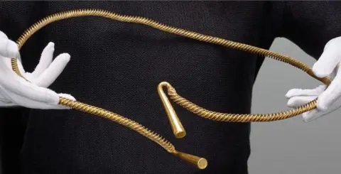 Trustees of the British Museum Bronze Age torc found in Cambridgeshire being held by a person wearing white gloves