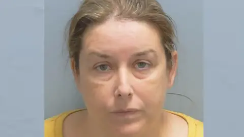 A custody photo shows Shelley Simpson with tied-back, light brown hair and wearing a yellow top.