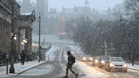 Reuters A man crosses a snowy junction with Princes Street in Edinburgh with Christmas tree in the distance during Storm Bert