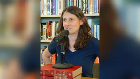 Woman speaking into a podcast microphone in front of a bookshelf