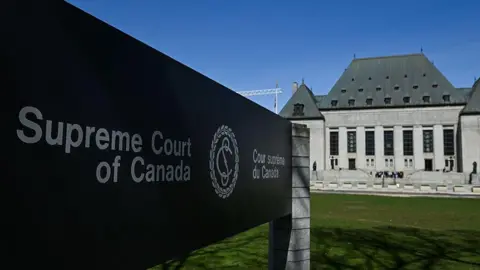 The Supreme Court of Canada sign in the foreground with the court building behind it. 