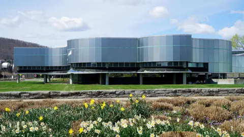 Corning Museum of Glass A horizontal grey glass building on stilts with daffodils in the foreground.