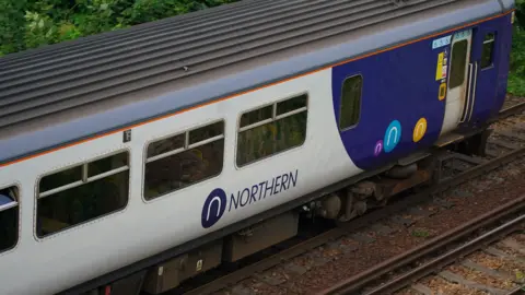 PA Media A Northern railway train with the grey and purple livery at Hunt's Cross station, Liverpool