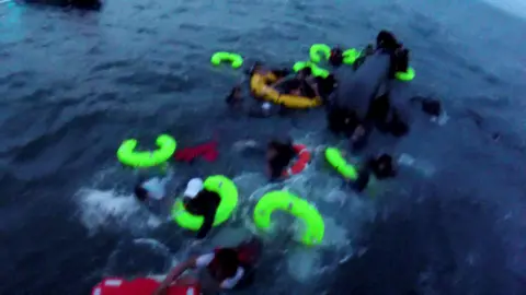 BBC yellow and red grammar in the sea while people try to stick to them. The image is a little blurry as it was taken from the body's camera.