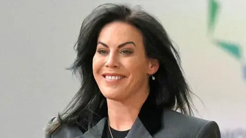 Getty Images Jennifer Carroll MacNeill is seen arriving at the European Union–Gulf Cooperation Council (GCC) summit in Brussels on October 16, 2024.
She has long black hair and is smiling. She is wearing a grey suit with black trim, a black T-shirt, and a silver necklace.