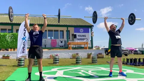 BBC/ Cara Thorpe Two men lift weights above their heads.