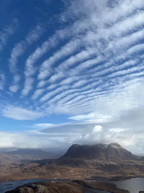Gordon O'Connor The view from a mountain on a sunny day with patterned clouds in the sky and another mountain in the distance 