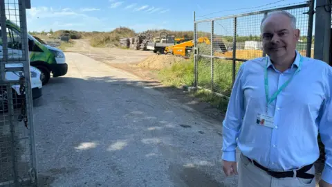 Councillor Ian Snowdon in front of the allotments site. Vehicles and rubble can be seen behind him.