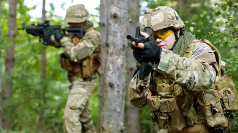 Getty Images Two UK Army soldiers in camouflage holding guns in the forest.