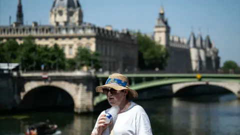 A woman with a hat cools off with a cold bottle of water on the Seine riverside