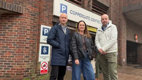 York BID Three people stand in front of Coppergate Multistorey car park. From left to right is York BID Executive Director Andrew Lowson, Bishopthorpe Road Traders' Association's Ruth Phillips and York High Street Forum Chair Phil Pinder.