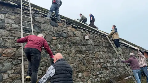 BBC eight people on ladders and the roof assessing dfamange and putting tiles back on.