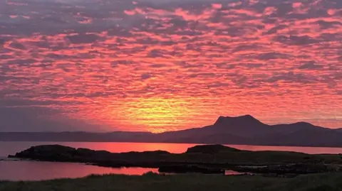 Debbie Webster A sunset over the water. Pink and yellow sunlight reflects off of rippling clouds and two islands create dark distinct shapes.