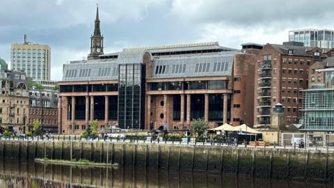 A red brick and glass court building on a riverside