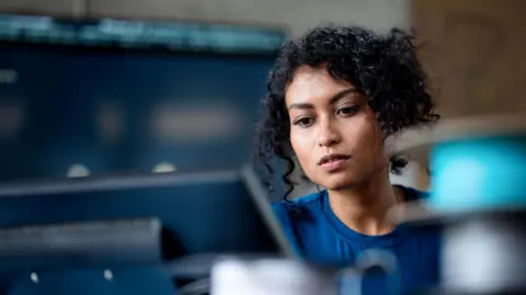 Getty Images A woman with dark hair works on laptop. She is wearing a blue top.