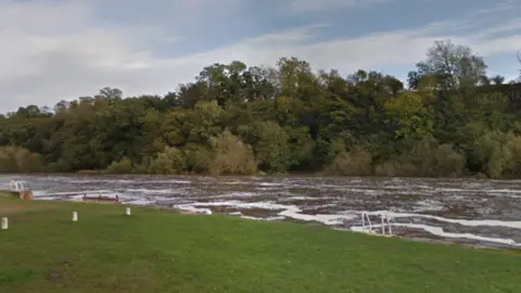 Google The River Trent at Gunthorpe Locke. There are white peaks on the rough water and 2 sets of steps down from the grass bank.