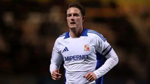 Will Wright looking forward while running and wearing Swindon Town's white and blue away kit