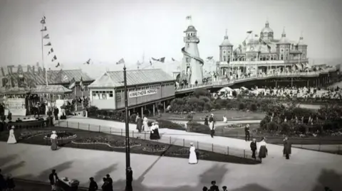 Great Yarmouth Borough Council A black and white image of the Britannia Pier as was rebuilt after the fire in 1868. It shows a turreted theatre or pavilion on the seaward end of the building, a helter-skelter and smaller kiosks and booths closest to the landward side.