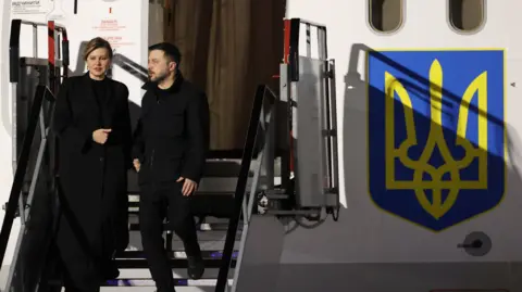 PA Media Volodymyr Zelensky and his wife Olena Zelenska disembark from plane stairs towards the runway at Dublin Airport. On the side of the plane is a yellow and blue Ukrianian symbol.